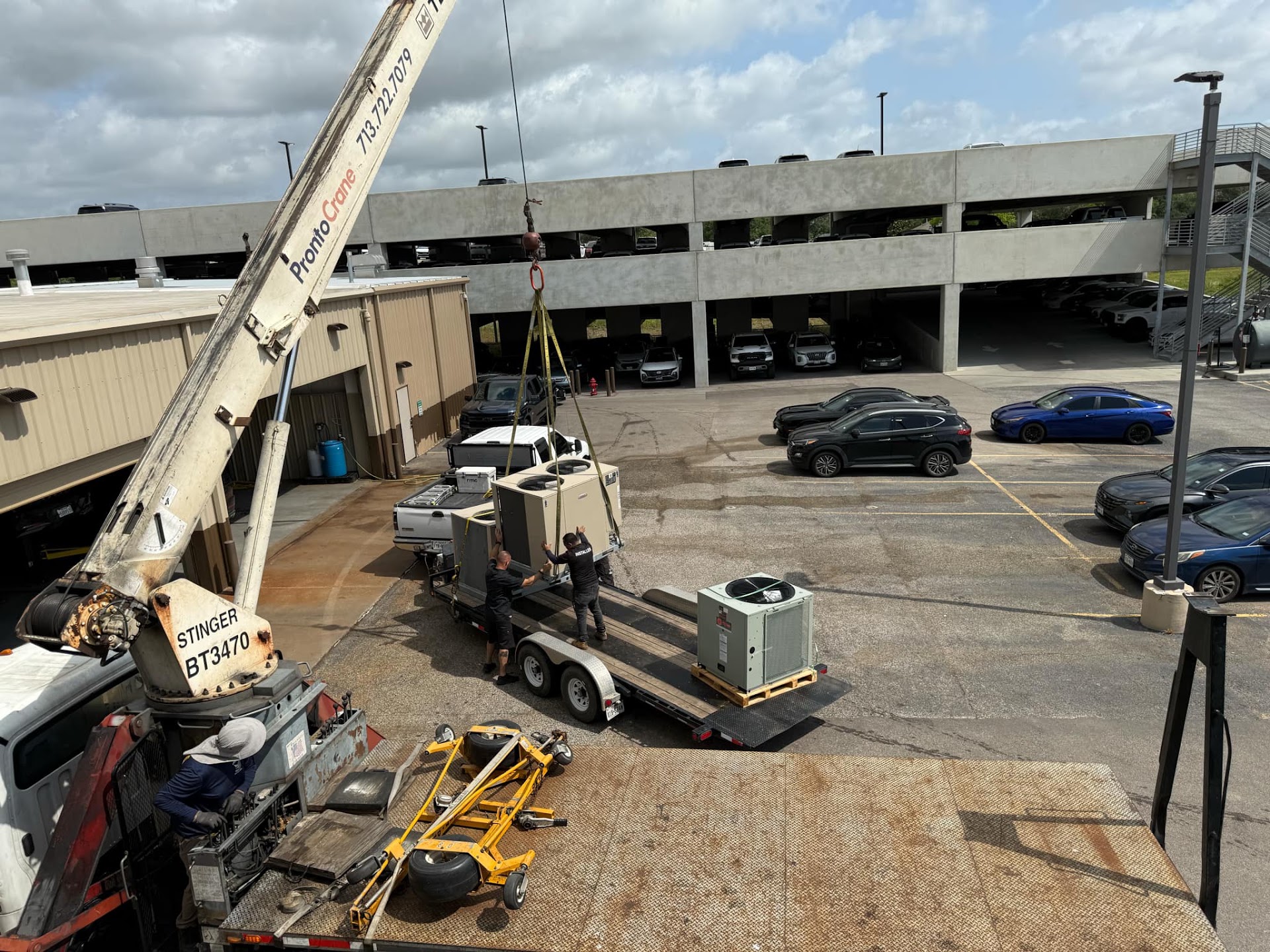 A crane lifting a packaged rooftop unit onto a trailer at a commercial job site