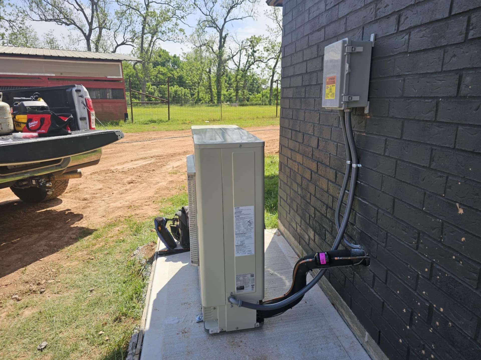A slim variable speed outdoor unit installed against a dark brick wall